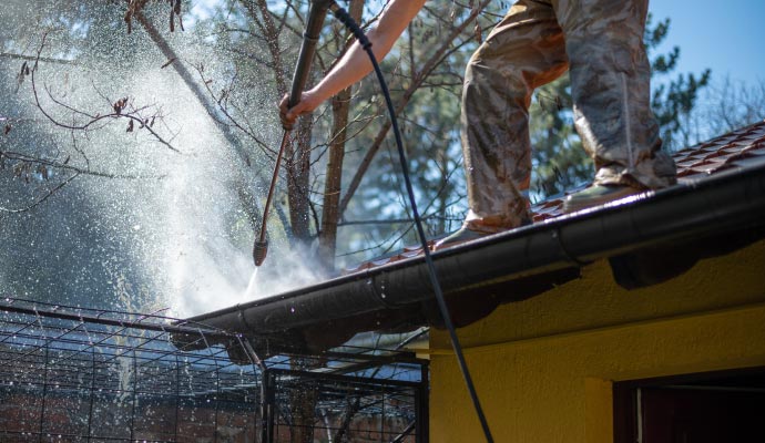 Person cleaning gutter with equipment
